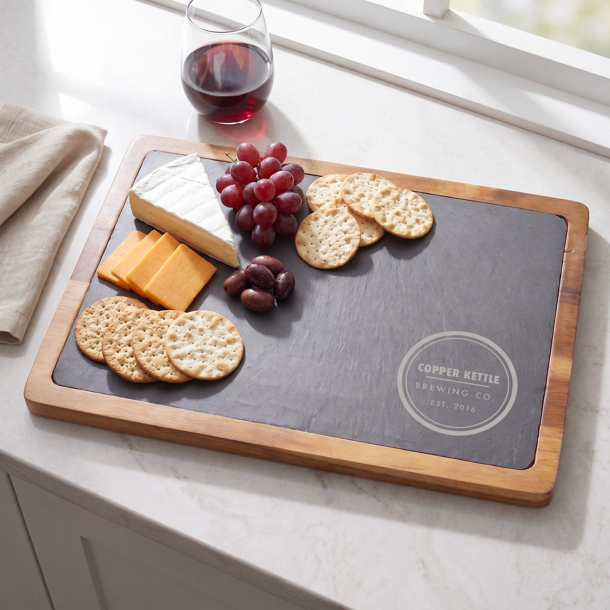 Logo engraved slate and acacia serving board with cheese and fruit