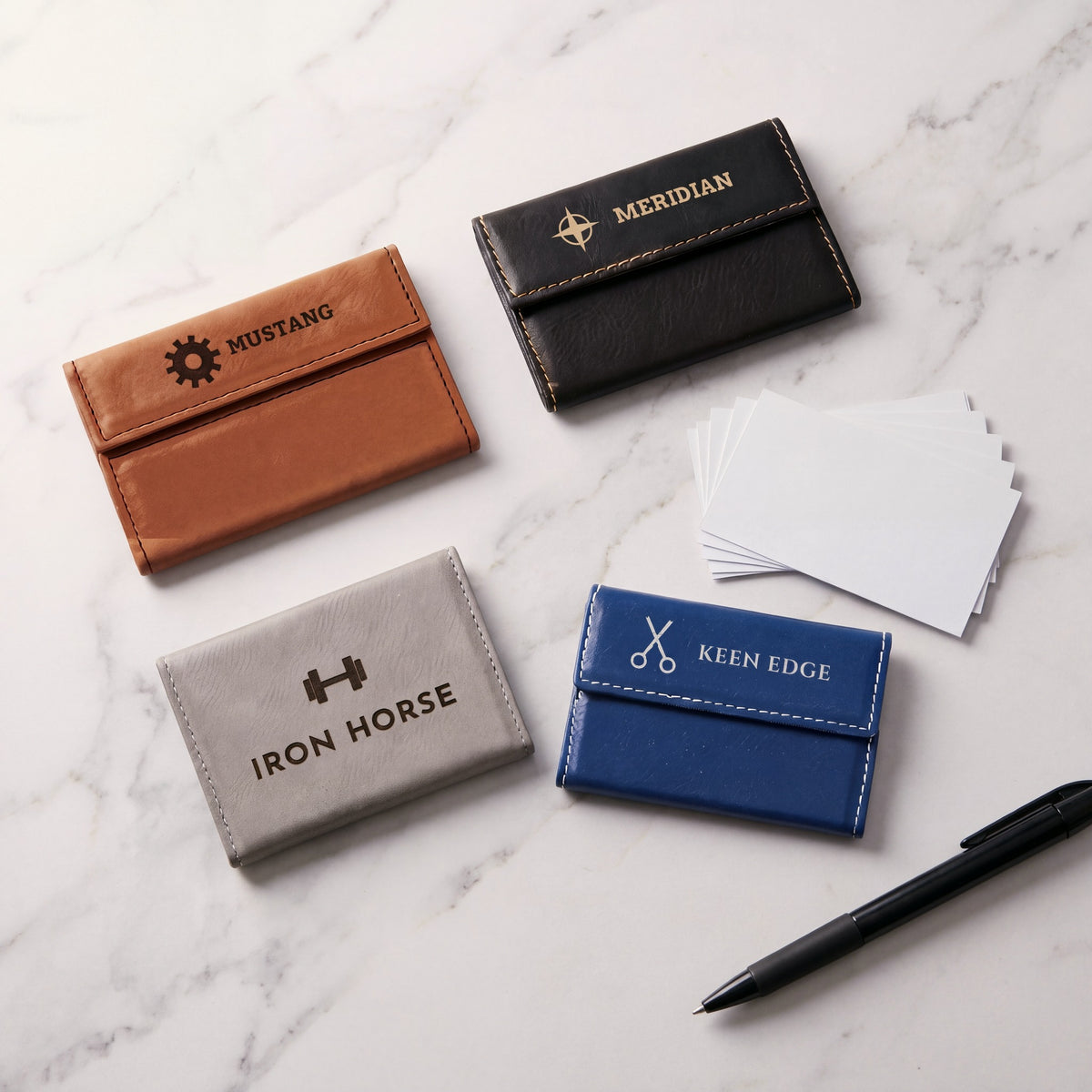 Custom Logo Leatherette Business Card Holders – rawhide, black/gold, gray and blue/silver holders on marble, each engraved with a different sample logo