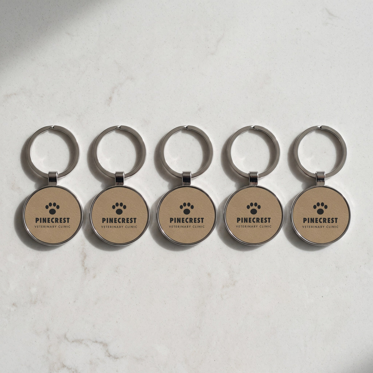 Custom Logo Leatherette & Metal Keychain – Round – bulk order of Light Brown keychains, all engraved with the same sample logo