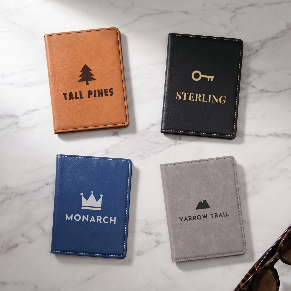 Custom logo leatherette passport holders in Rawhide, Black/Gold, Blue/Silver and Gray, each engraved with a sample logo, on white marble