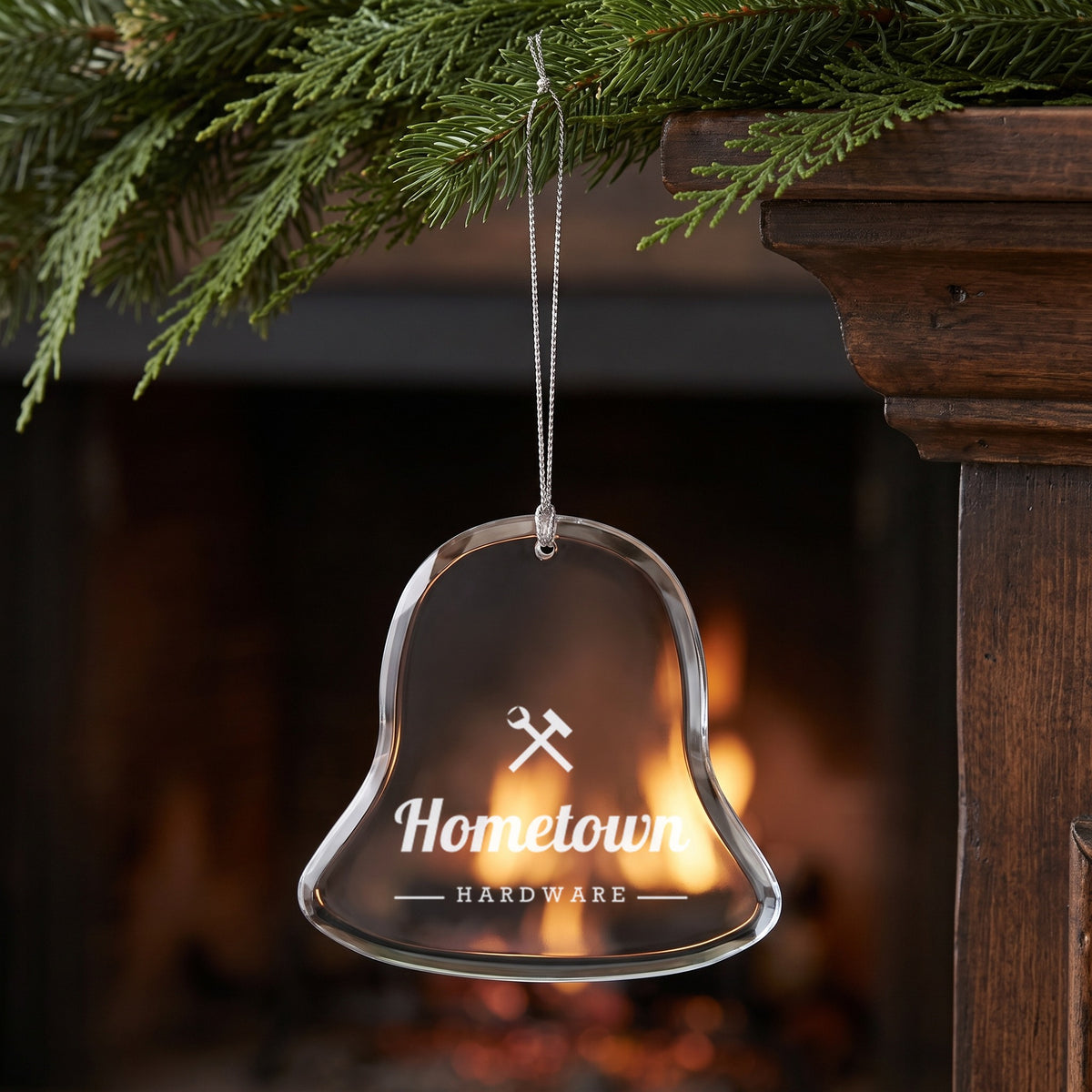 Custom Logo Glass Christmas Ornament, bell shape with an engraved sample hardware store logo over a fireplace