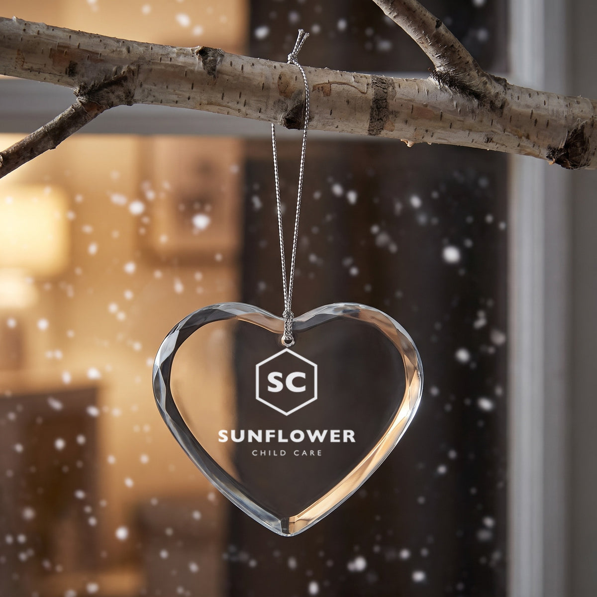 Custom Logo Glass Christmas Ornament, heart shape with an engraved sample child care logo hanging in a window
