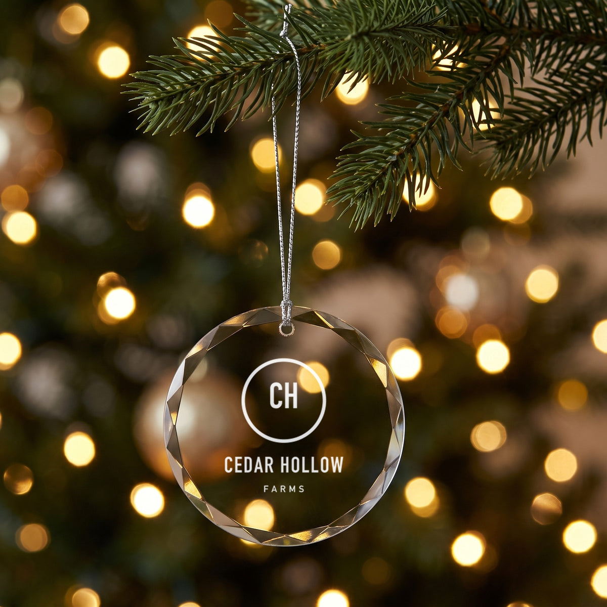 Custom Logo Glass Christmas Ornament, round clear glass with an engraved sample farm logo hanging on a Christmas tree
