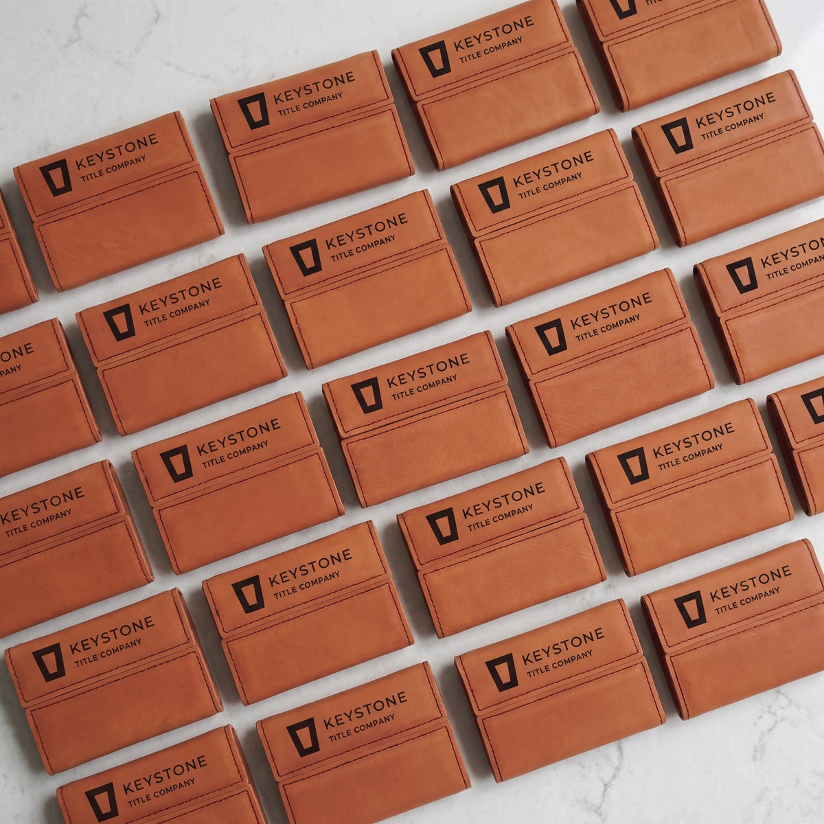 Custom Logo Leatherette Business Card Holder – bulk order of Rawhide holders laid out in rows, all engraved with the same sample logo