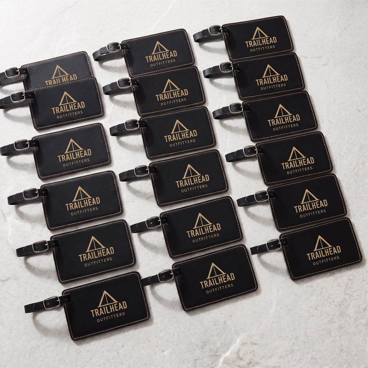 Custom Logo Leatherette Luggage Tag – bulk order of Black/Gold tags laid out in rows, all engraved with the same sample logo