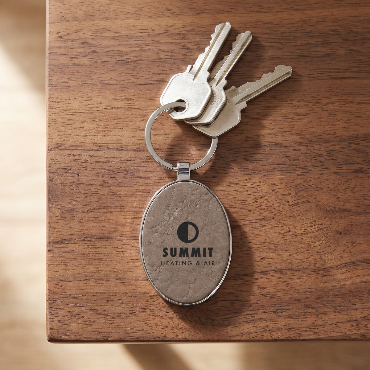Custom Logo Leatherette & Metal Keychain – Oval, Gray on a key ring with house keys, engraved sample logo