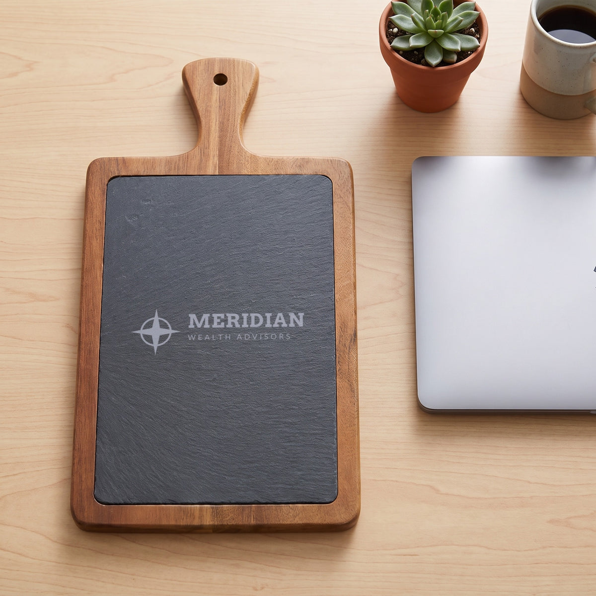 Custom Logo Slate & Acacia Paddle Cutting Board, 13 1/4 x 7 inch board with an engraved sample logo on an office desk as a client gift
