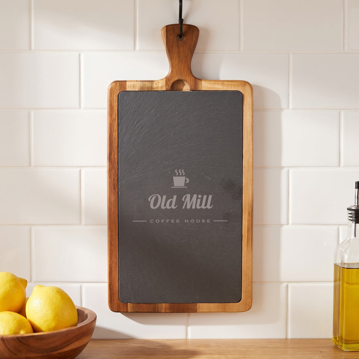 Custom Logo Slate & Acacia Paddle Cutting Board, engraved sample logo, hanging by its handle in a kitchen